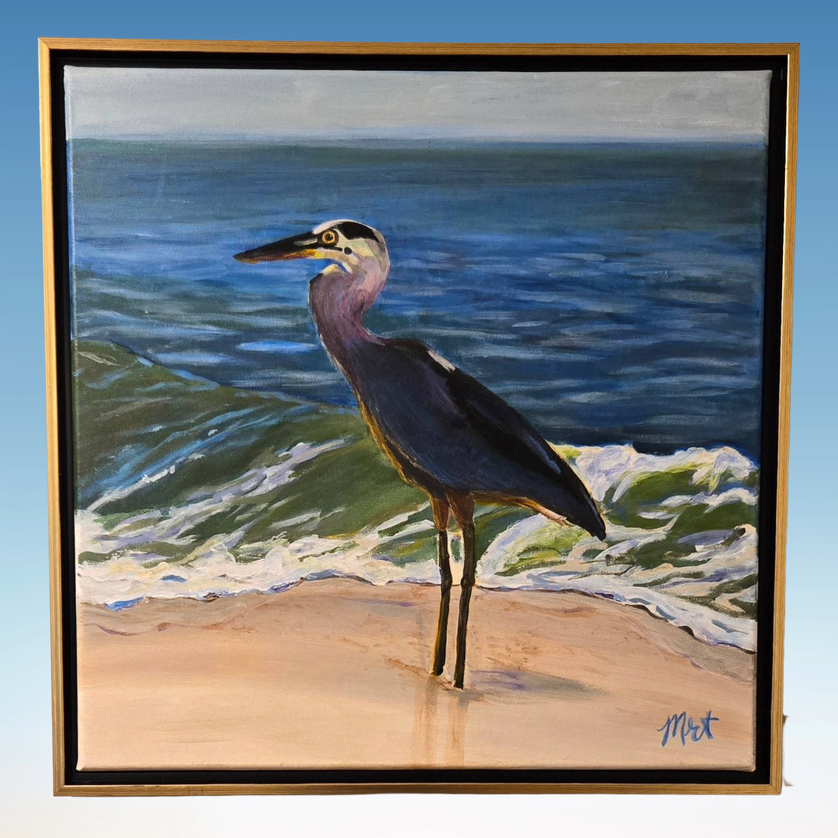 Acrylic painting of a great blue heron on the beach before ocean waves by Melanie Toudouze, shown in a gold frame